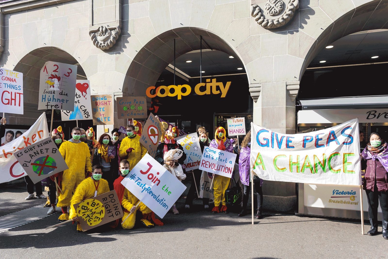 A crowd in chicken costumes with protest signs outside the Coop City entrance